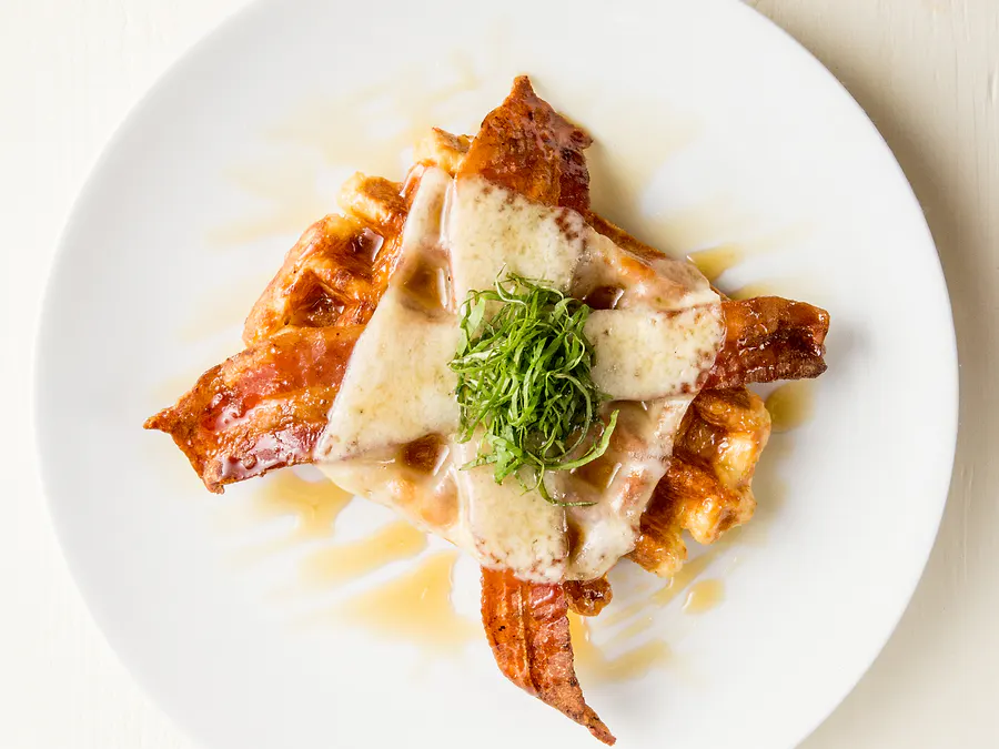 Liège waffle topped with bacon, melted havarti and fresh basil on a white plate