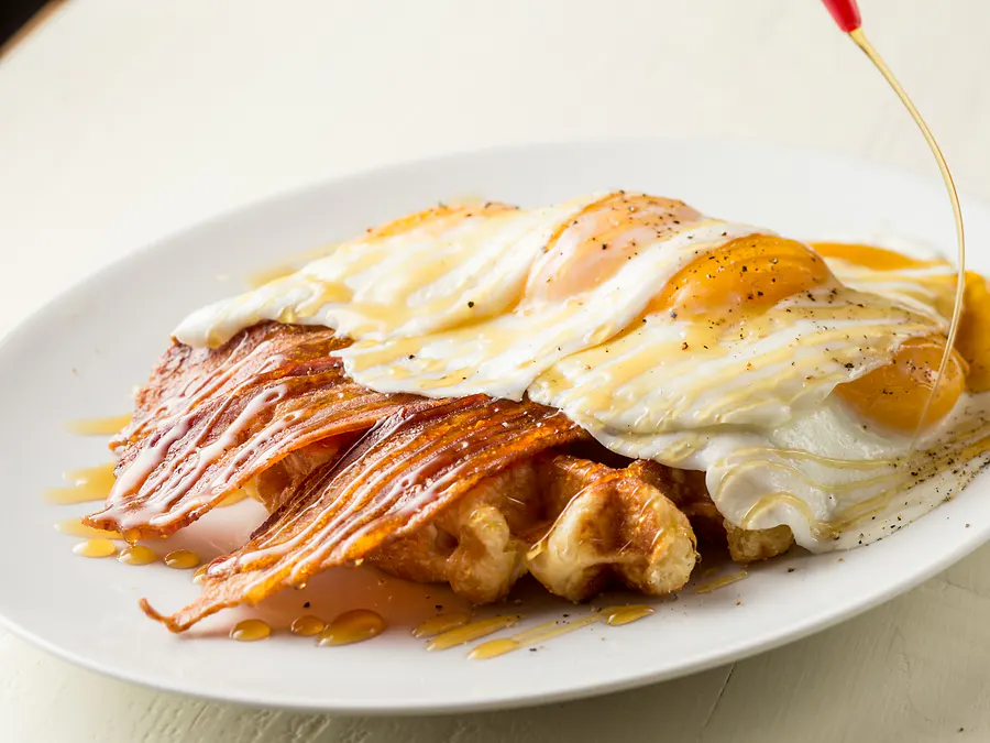 Large Liège waffle covered with four sunny side up eggs and four strips of bacon